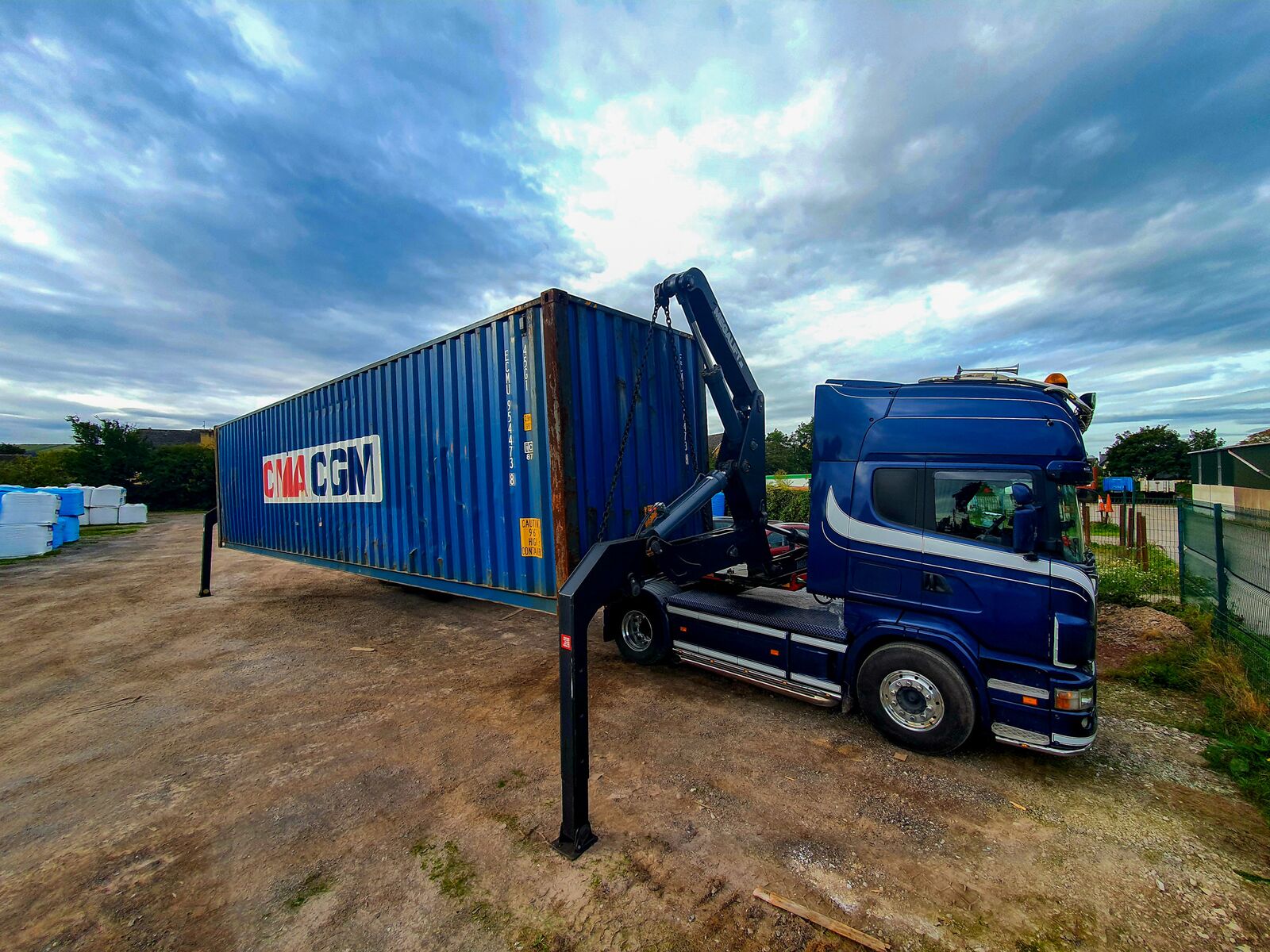 FMC Haulage Scania with Megalift side-loader trailer setting down a CMA CGM container on bare ground at a site with no crane or forklift