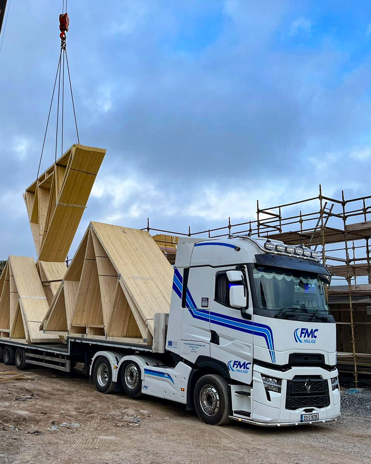 FMC Renault flatbed delivering timber roof trusses to a construction site with crane